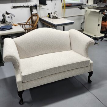 Chippendale loveseat sofa featuring cream-colored diamond patterned jacquard fabric and dark hand-carved cabriole legs in a professional workshop