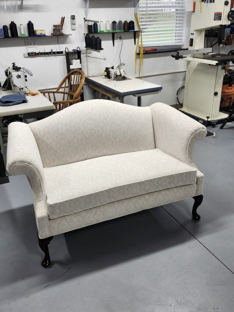 Chippendale loveseat sofa featuring cream-colored diamond patterned jacquard fabric and dark hand-carved cabriole legs in a professional workshop