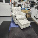 Antique recliner chair and ottoman featuring a cream and gold botanical patterned fabric with dark hand-carved wooden legs in a professional shop.