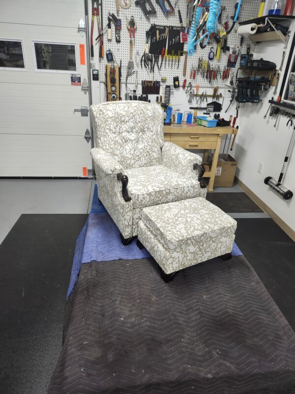Antique recliner chair and ottoman featuring a cream and gold botanical patterned fabric with dark hand-carved wooden legs in a professional shop.