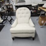 Vintage chair reupholstery featuring a high-back armchair with cream-colored textured fabric and button tufting in a professional workshop
