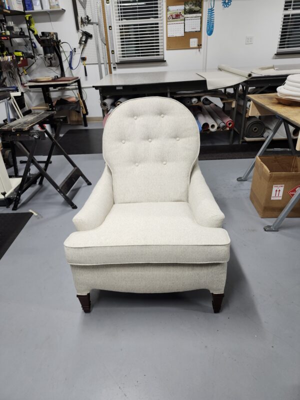 Vintage chair reupholstery featuring a high-back armchair with cream-colored textured fabric and button tufting in a professional workshop