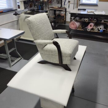 Vintage child recliner chair featuring a textured light-blue fabric with dark-stained wooden arms and base in a professional shop
