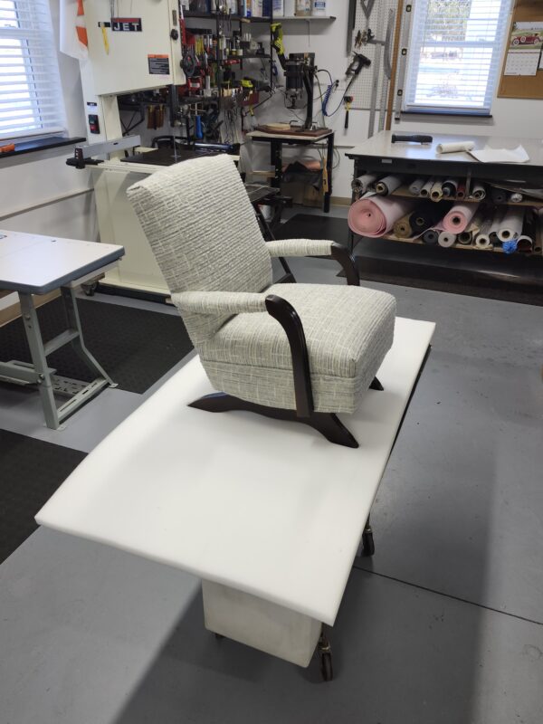 Vintage child recliner chair featuring a textured light-blue fabric with dark-stained wooden arms and base in a professional shop