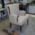 Mid-60s channel back chair featuring light grey textured fabric with precision vertical channels and decorative nailhead trim