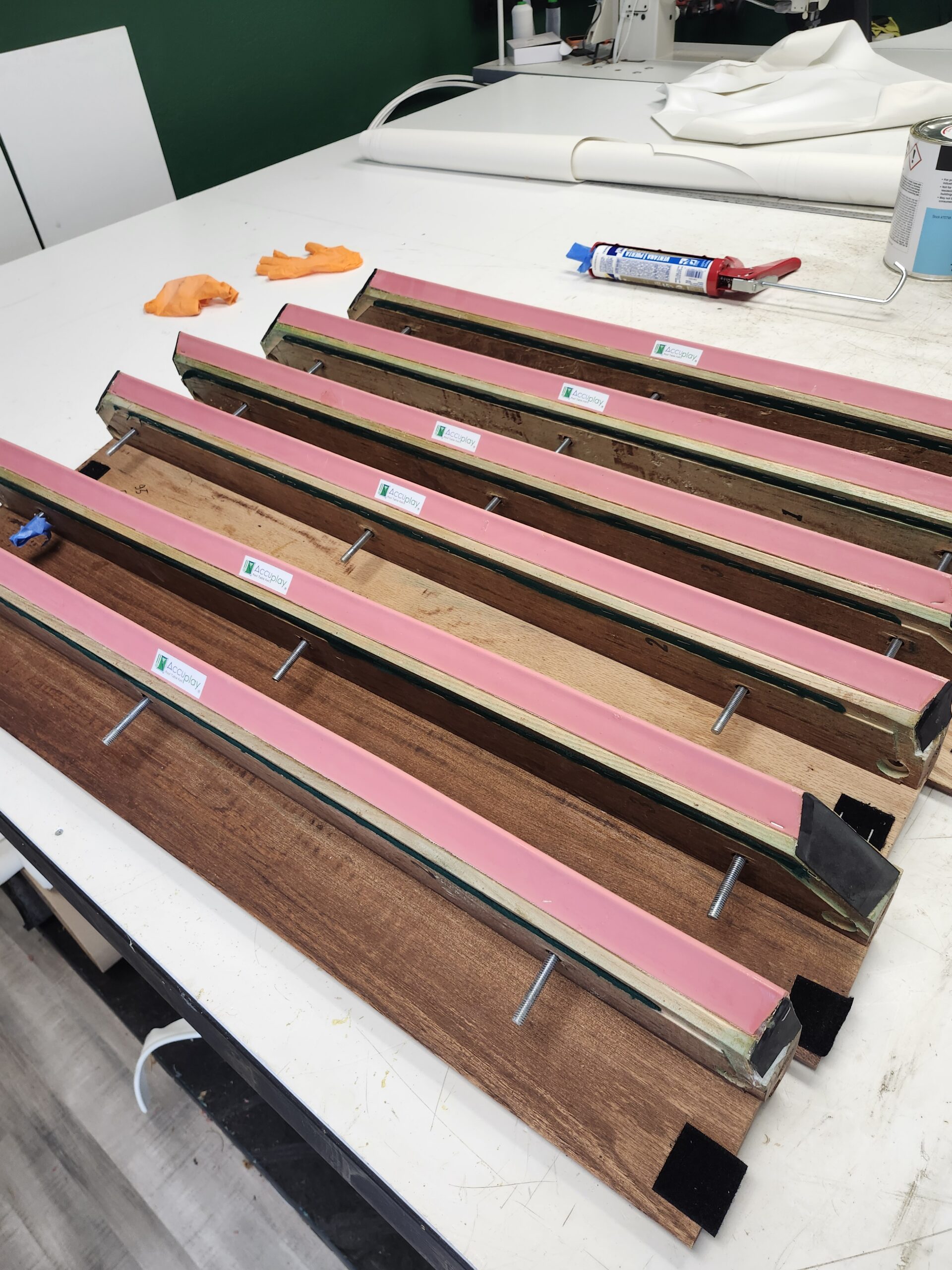 New K-style pool table cushion rubber glued to six oak rails, factory labels still attached, adhesive curing on the bench