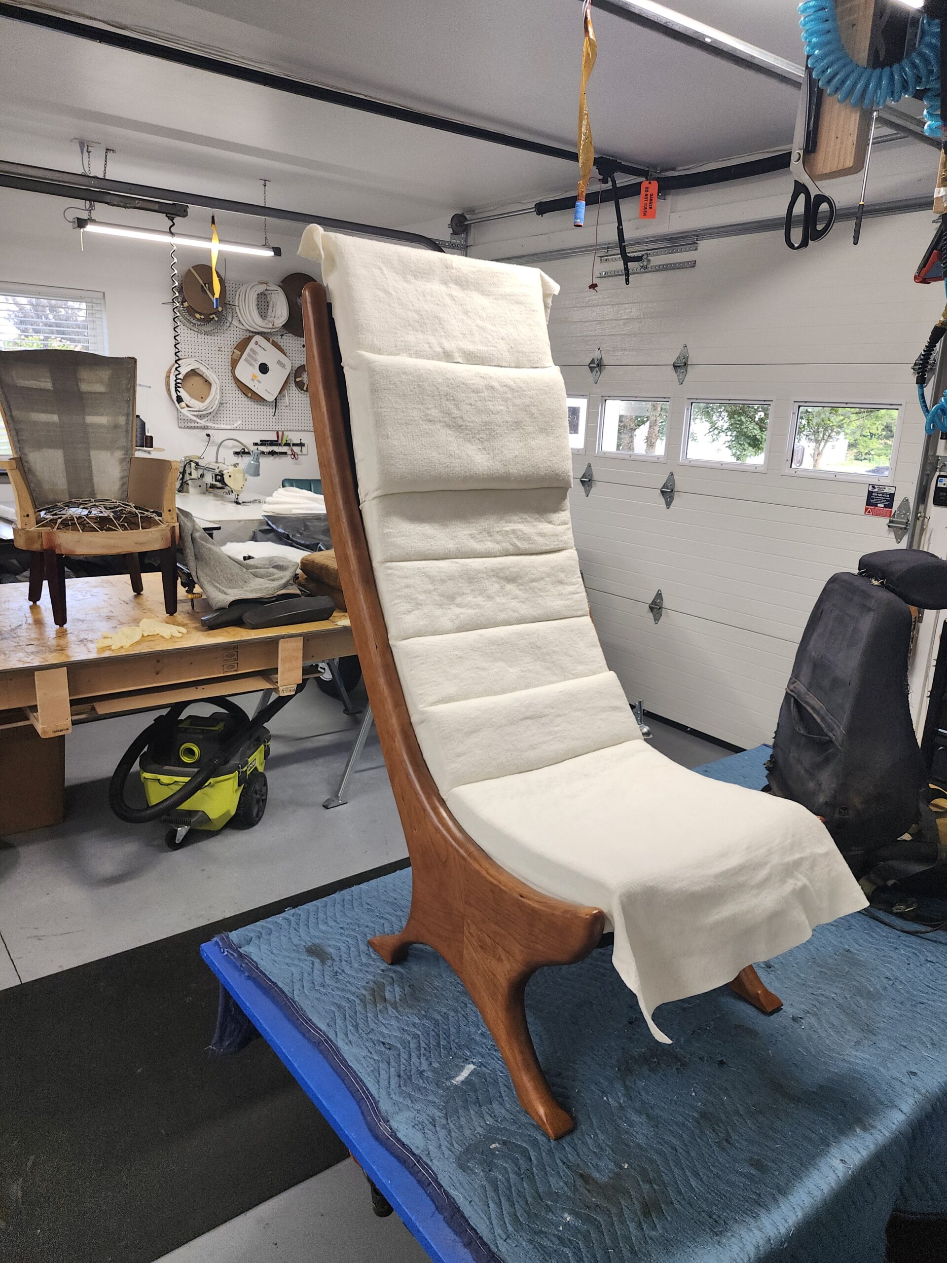 High-back bentwood chair frame with fresh white foam and batting layers built over the wooden slat deck during the padding stage