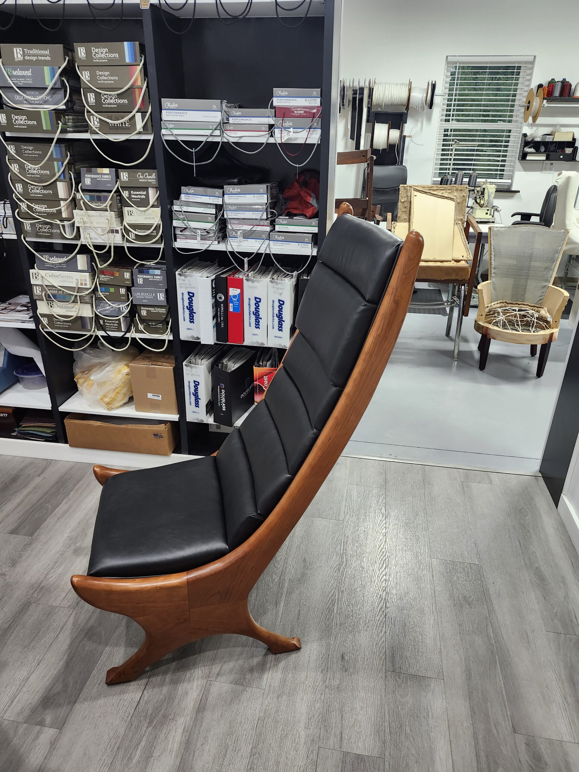 Side profile of the finished high-back lounge chair showing the dramatic bentwood curve wrapped in channeled black leather
