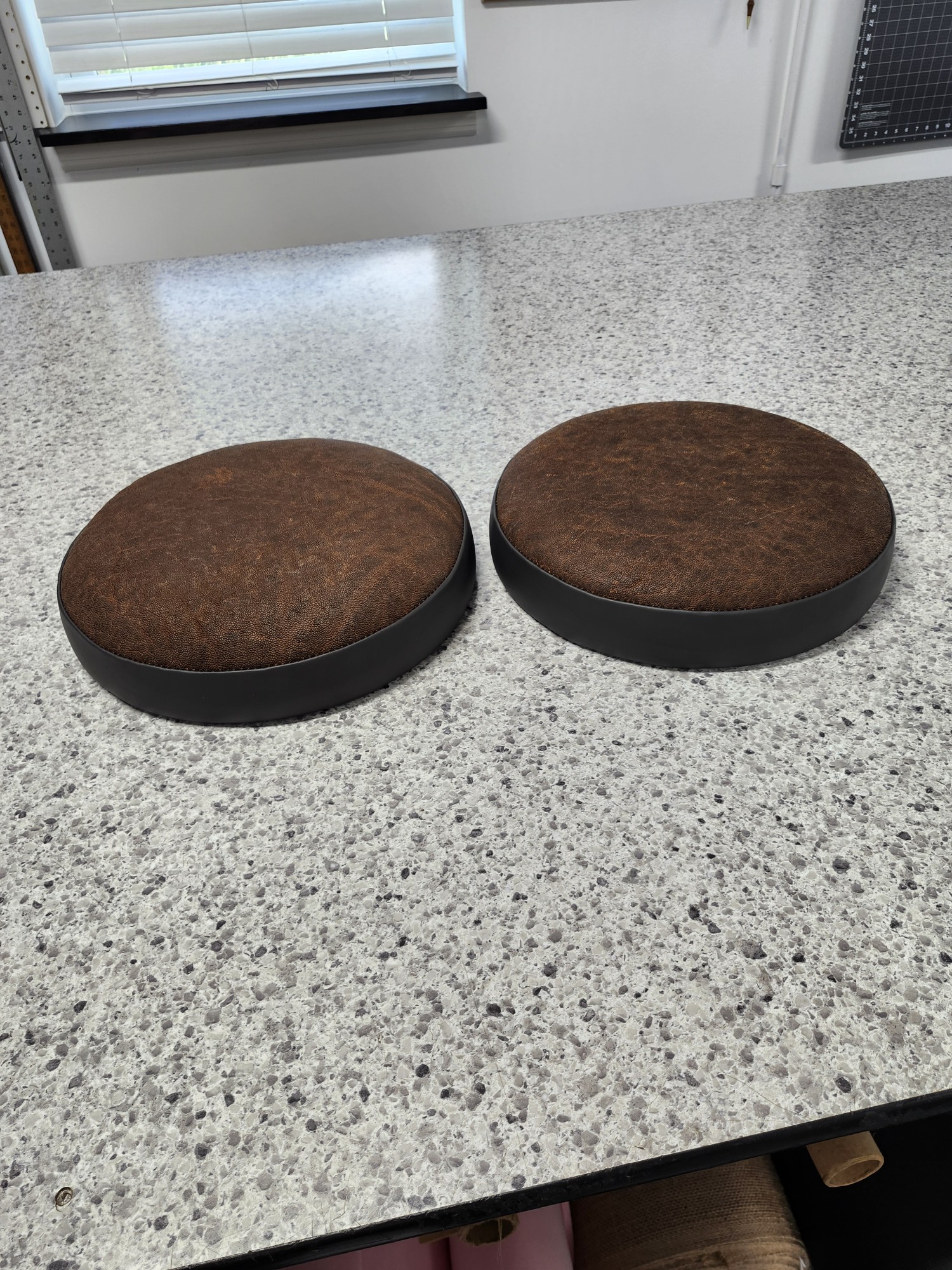 Pair of round brown elephant leather stool seat cushions with black boxing bands on the workbench