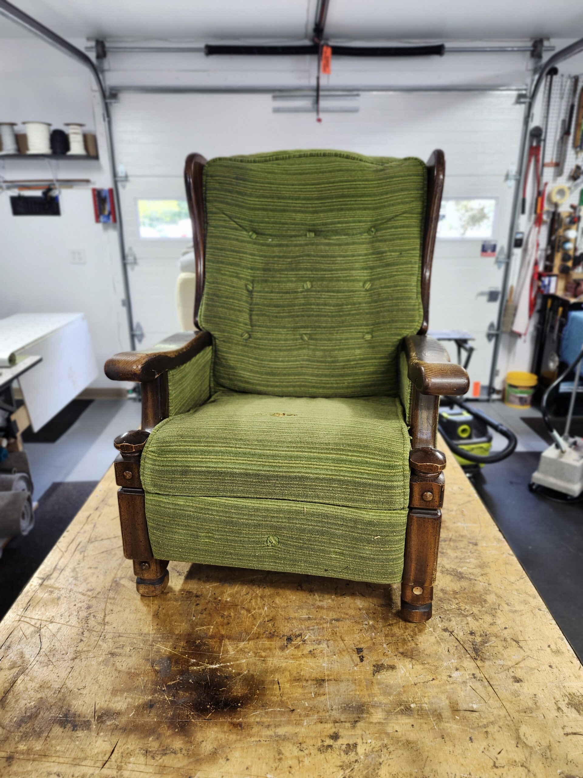 Vintage recliner reupholstery Reading PA project: wood arm wing recliner in worn green striped fabric with a hole in the seat, before reupholstery at Alex Upholstery Shop