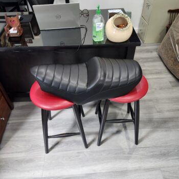 Long tapered motorcycle saddle recovered in black vinyl with horizontal tuck and roll pleats at Alex Upholstery Shop