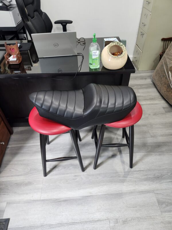 Long tapered motorcycle saddle recovered in black vinyl with horizontal tuck and roll pleats at Alex Upholstery Shop