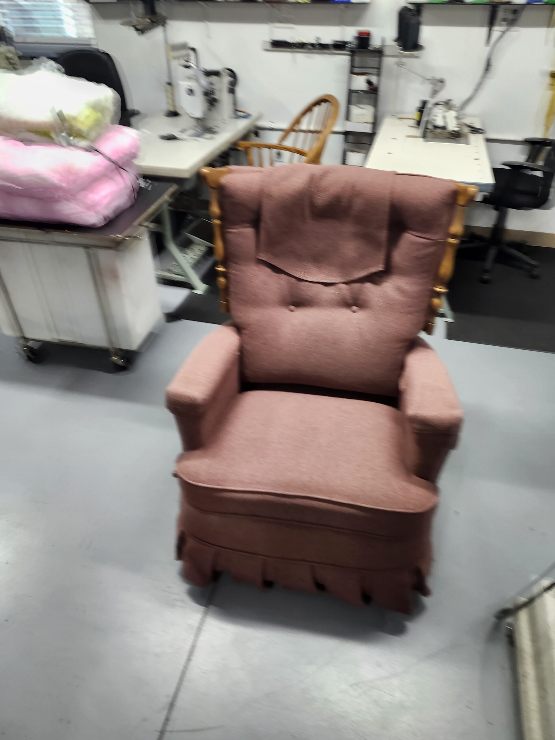Mid-century La-Z-Boy recliner before reupholstery in worn dusty rose fabric with a loose headrest cover draped over the back, two buttons, padded arms, pleated skirt and turned wood posts, on the floor at Alex Upholstery Shop