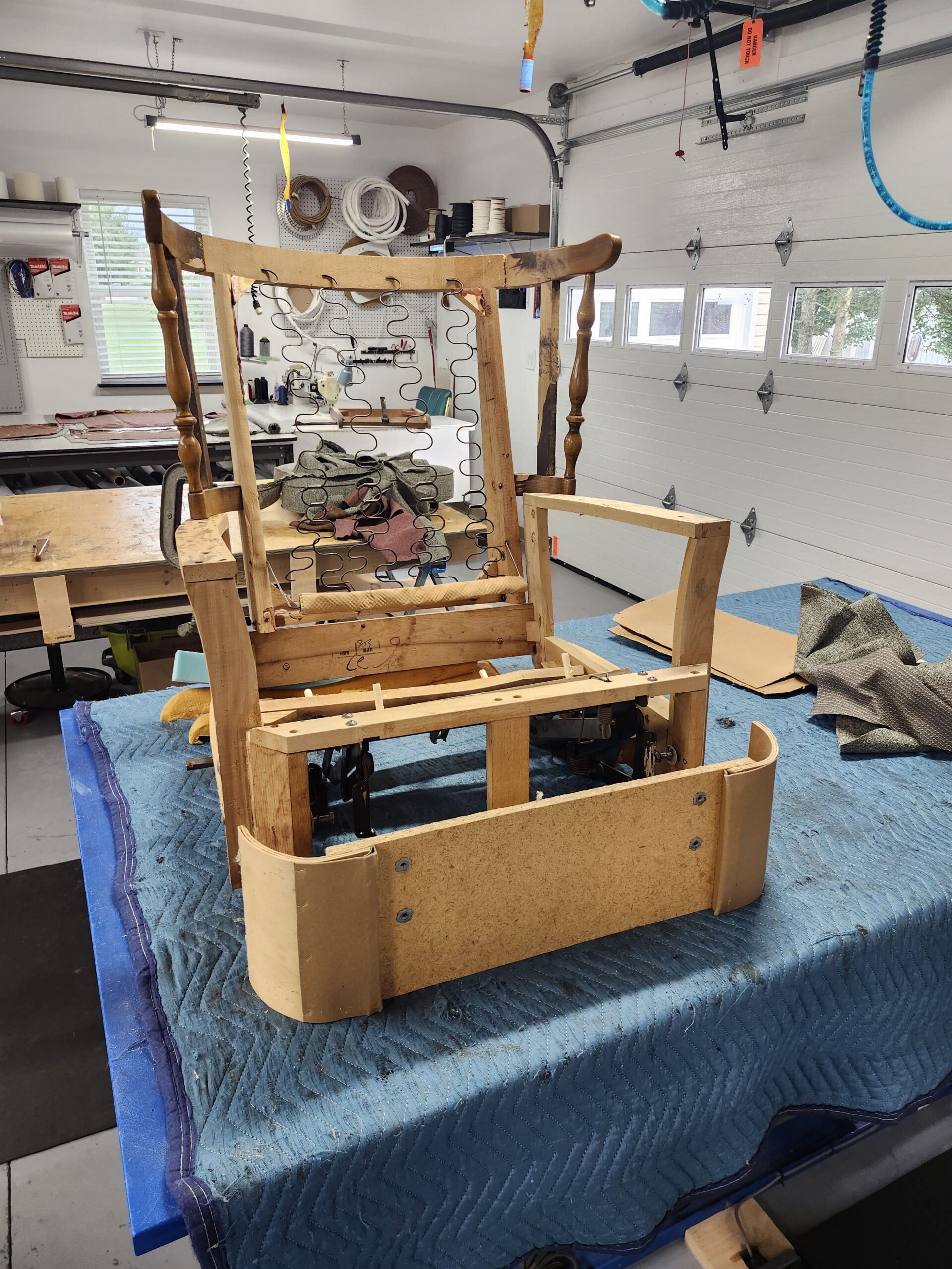 La-Z-Boy recliner stripped to the bare wood frame on a blue moving blanket, showing the turned posts, sinuous springs in the back, the steel reclining mechanism under the seat and new curved plywood arm panels screwed in place