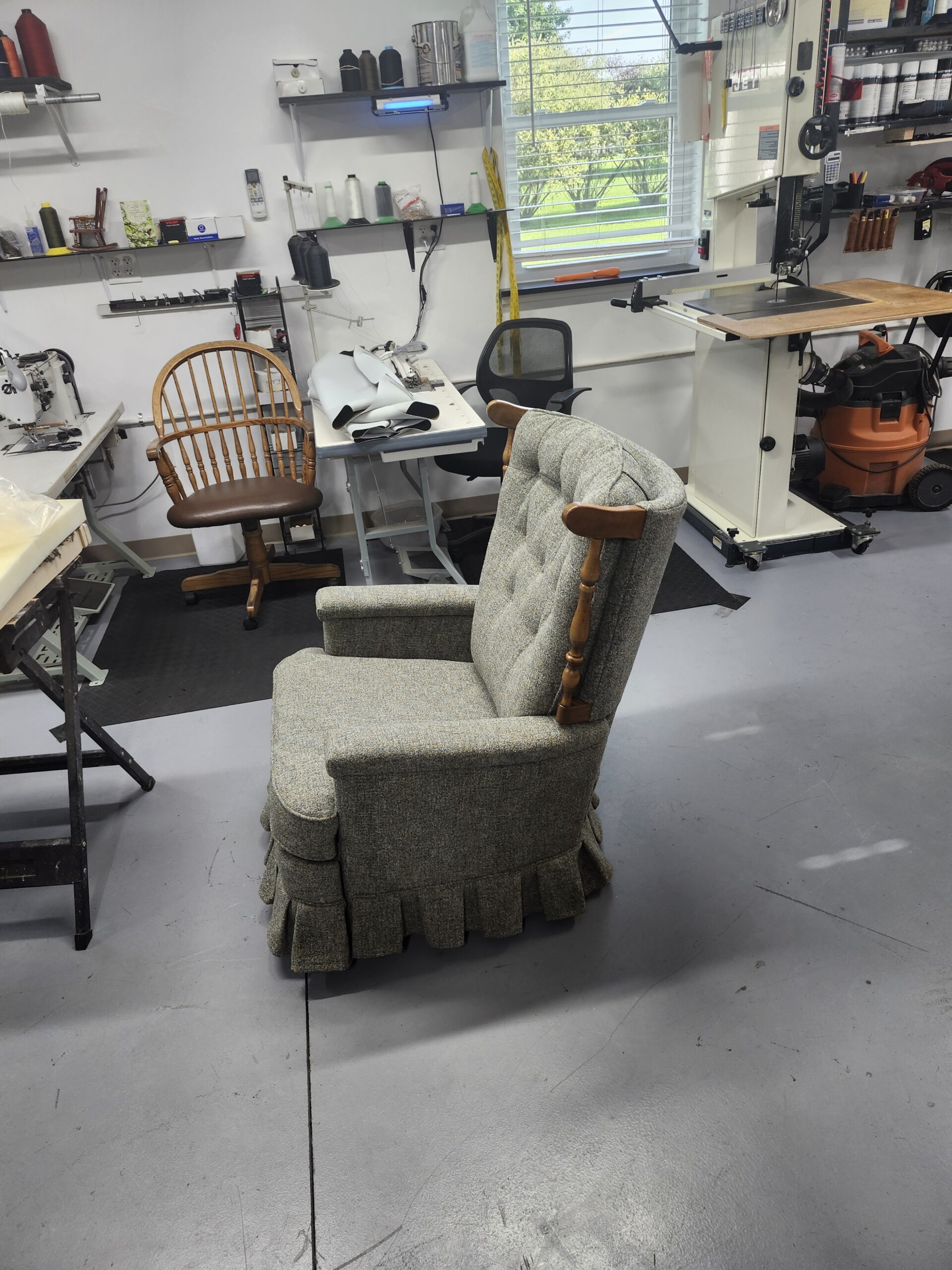 Side profile of the reupholstered mid-century La-Z-Boy recliner in gray-green tweed showing the turned wood post with its curved cap, the padded arm and the pleated box skirt