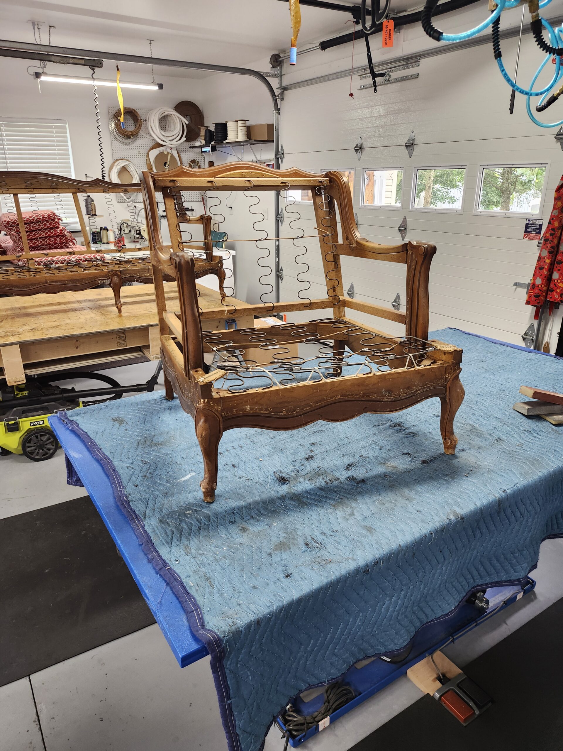 The same French Provincial chair stripped to its bare carved wood frame showing sinuous zigzag springs in the seat and back, worn finish and old tack holes along the rails