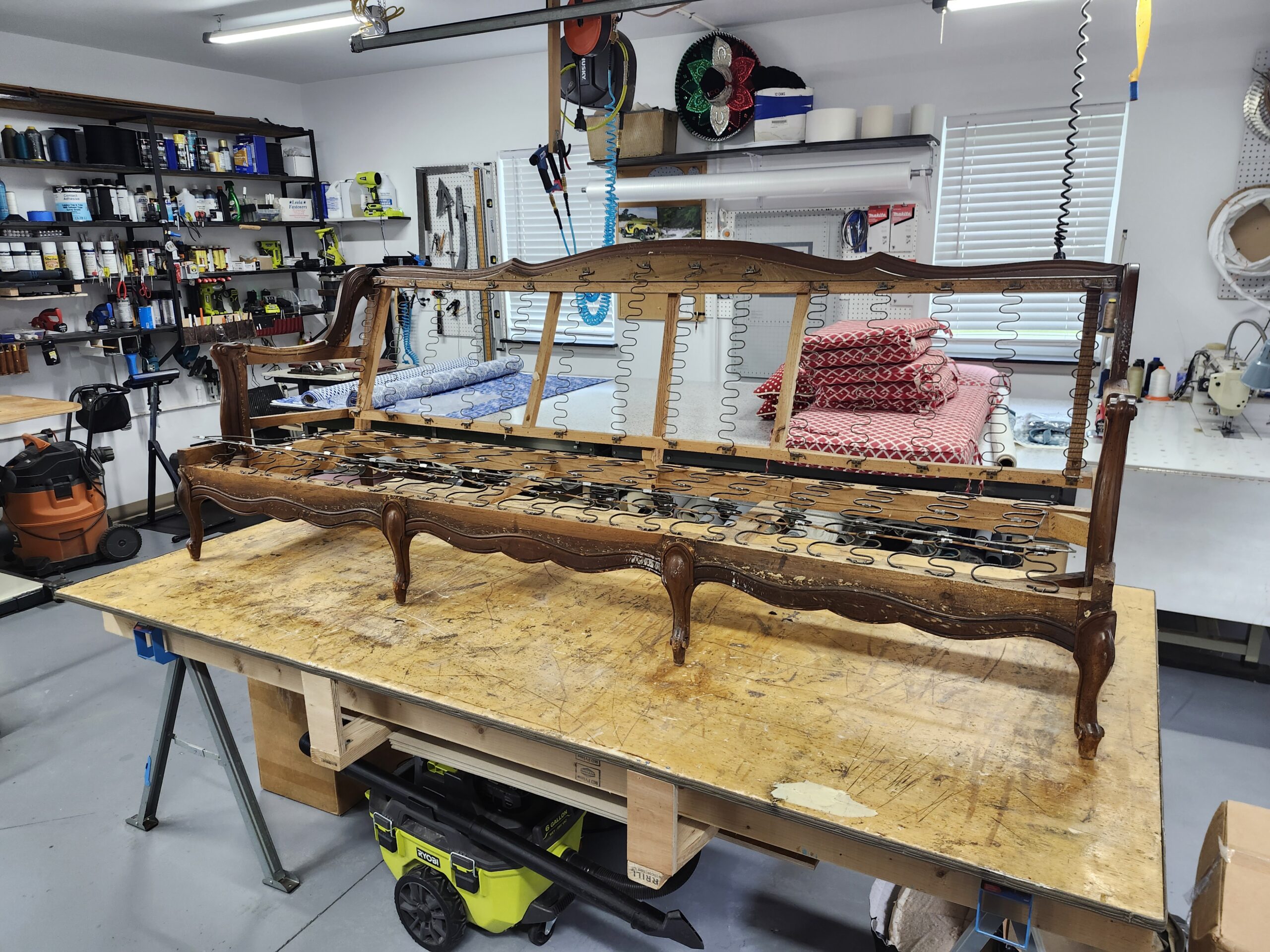 French Provincial sofa frame stripped bare on the workbench with sinuous springs across the full seat deck and up the back, carved serpentine crest rail, scalloped apron and cabriole legs