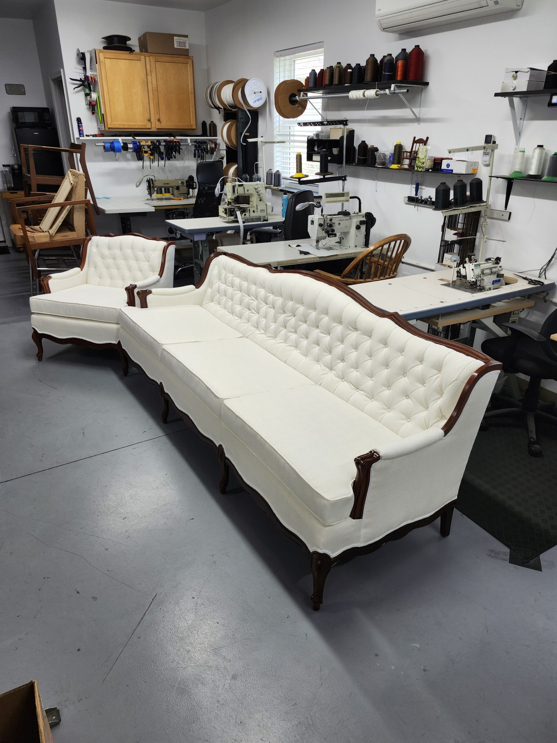 Finished French Provincial sofa seen from its end with the matching chair behind it, ivory diamond tufting, welted cushion edges, scrolled wood arm front and refinished cabriole leg in the Alex Upholstery Shop workroom