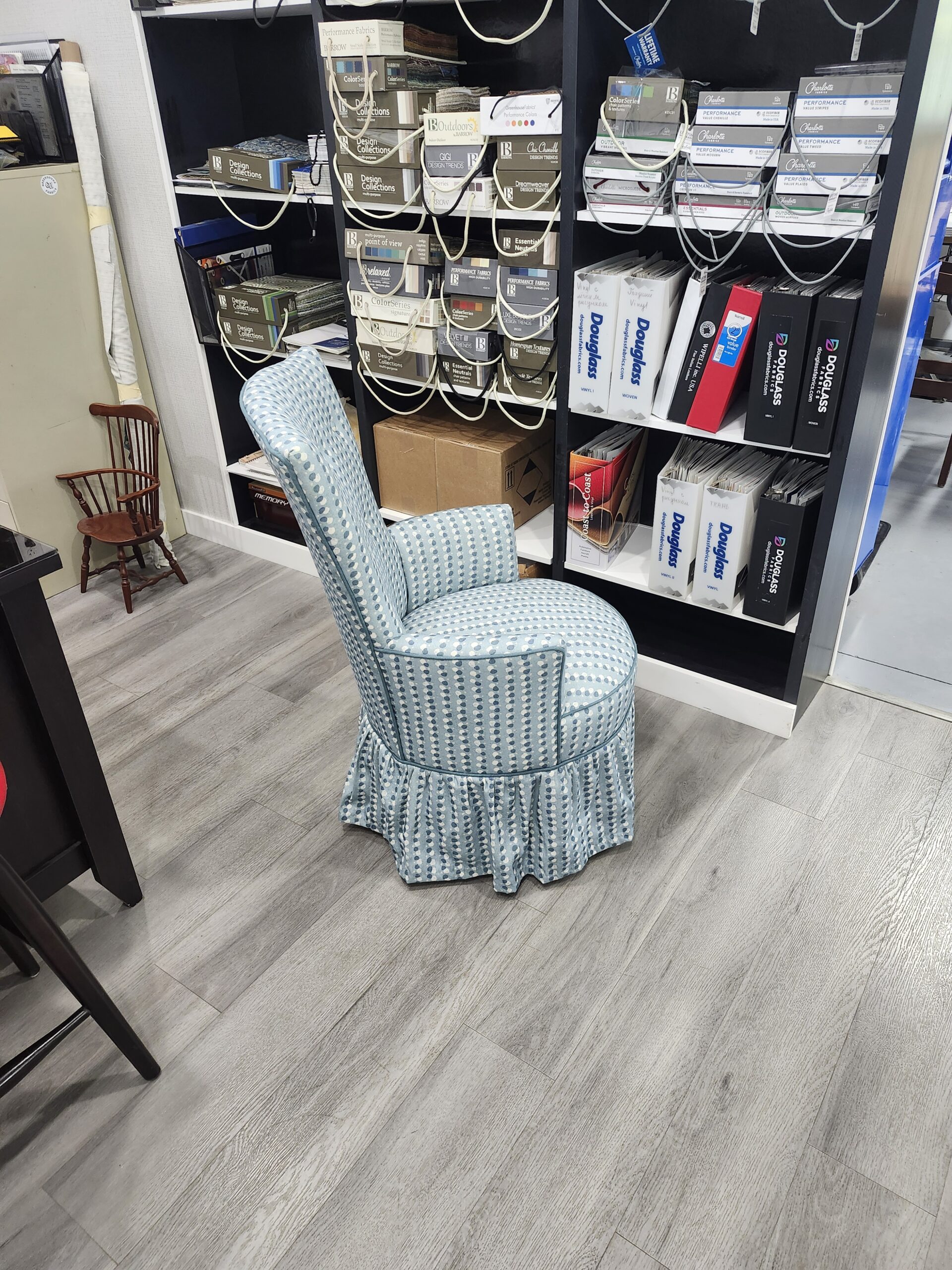 Side profile of the reupholstered round slipper chair showing the tall slim back, the round welted seat overhanging the piped skirt seam and the small scrolled arm, in the Alex Upholstery Shop showroom