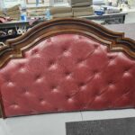 Headboard upholstery Mechanicsburg PA project: finished arched wood headboard with a diamond button tufted panel in oxblood pull-up leather, standing on the floor at Alex Upholstery Shop